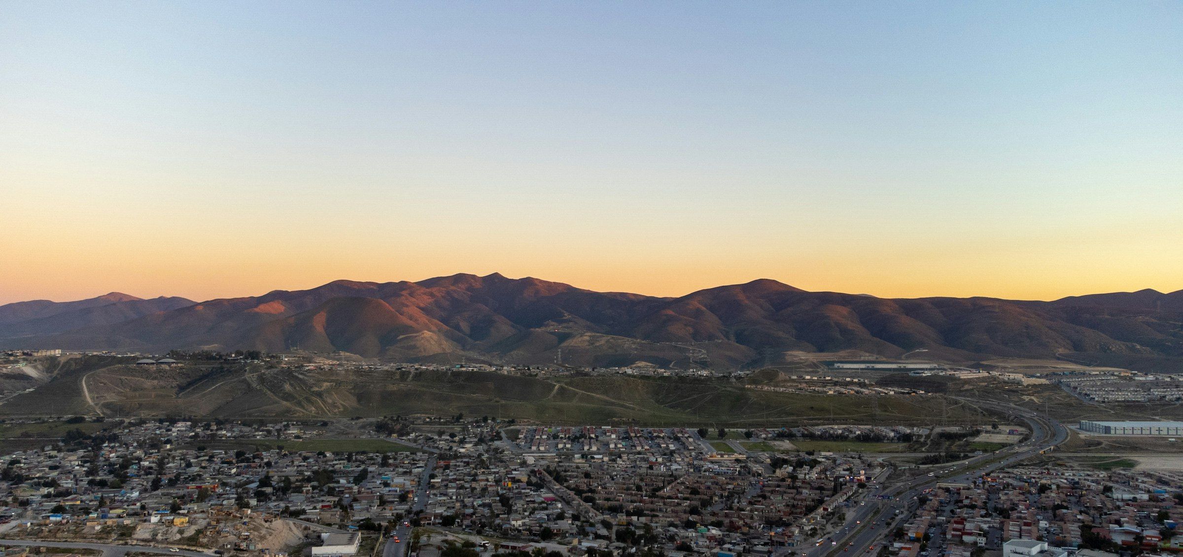 Tijuana al atardecer: la ciudad extendida entre cerros bajo un cielo naranja.